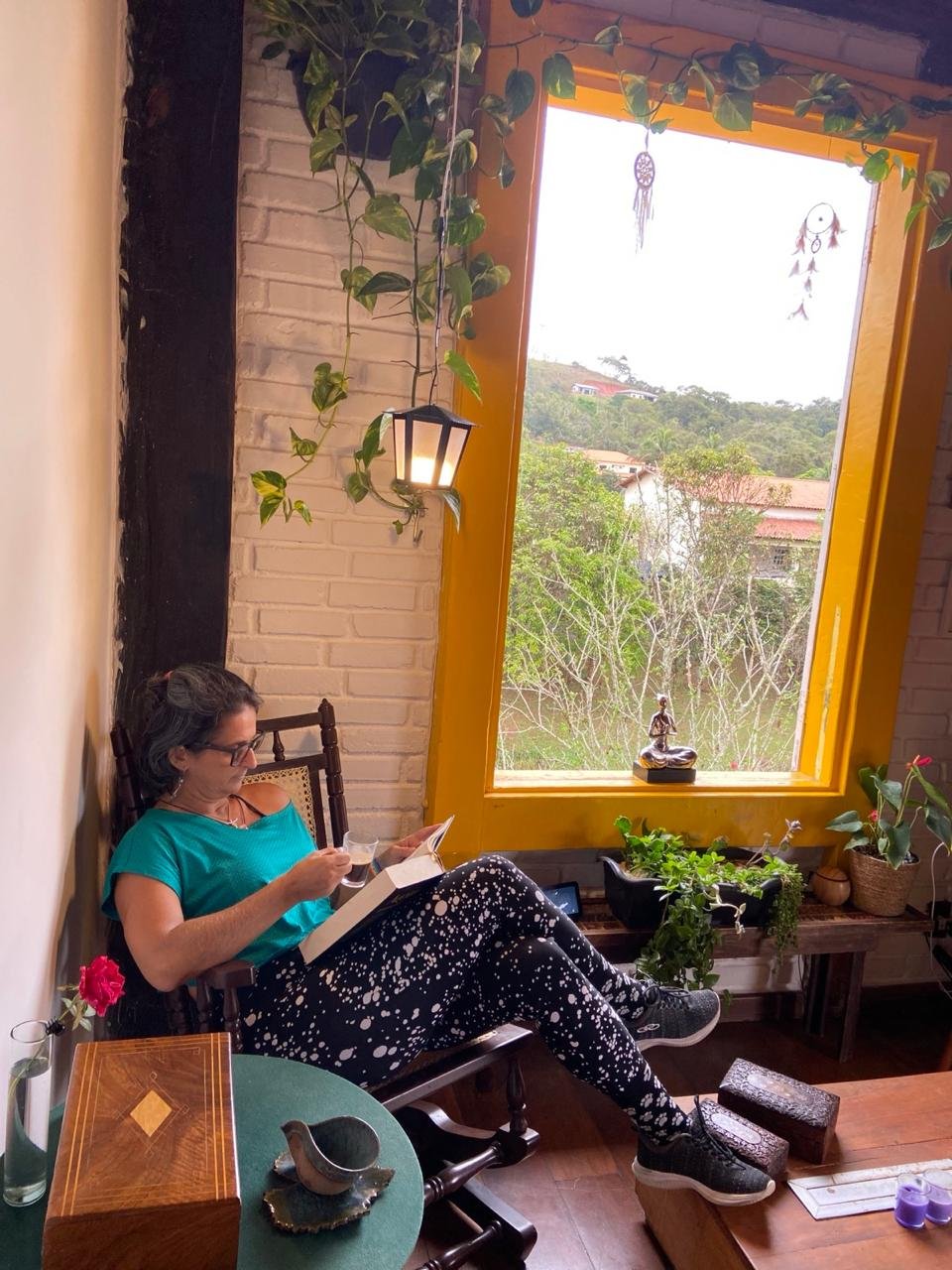 Dany Ribeiro lendo em um ambiente com plantas e janela aberta